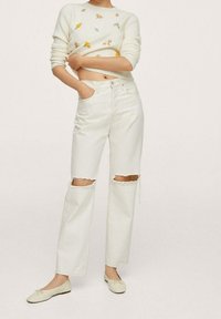 Pull court blanc avec broderies florales associé à un jean blanc taille haute aux genoux déchirés. Des chaussures plates blanches complètent la tenue.