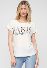 T-shirt en coton blanc à manches courtes et encolure ronde, affichant "PARIS" en imprimé léopard et "Restez Différent" en script noir en dessous.