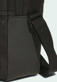 Černá textilní taška se hladkým pevným dnem a tkaným popruhem, vybavená zipovým zapínáním a prošíváním.