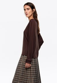 Bruine lange mouw top met een relaxte pasvorm, gecombineerd met een geruite rok in aardetinten. De stof lijkt glad met een lichte glans.