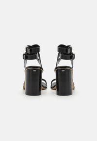 Sandalias negras de tacón con un diseño elegante, dos tiras en el tobillo, un tacón bloque texturizado y estilo de punta abierta. Acabado de material suave.