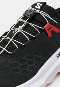 Μαύρο αθλητικό παπούτσι με υφαντό επάνω μέρος, ανακλαστικά κορδόνια, κόκκινες λεπτομέρειες και λευκή μαλακή σόλα. Διαθέτει σύστημα ασφαλούς εφαρμογής.
