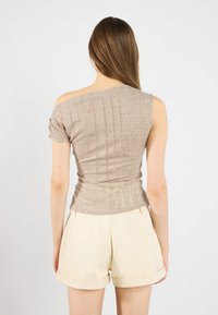 Beige neulepaita, jossa on lyhyet hihat, epäsymmetrinen pääntie, tekstuuri ja istuva siluetti, yhdistetty vaaleisiin shortseihin.