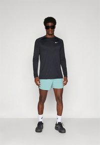 Must pikkade varrukatega spordipluus tekstureeritud kangaga ja Nike logoga, seljas helesinised lühikesed püksid, mustad tossud ja tumedad päikeseprillid.