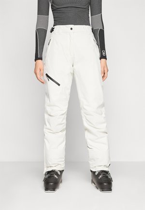 Pantalons de ski blancs à coupe décontractée, dotés de poches zippées et de coutures renforcées. Associés à des bottes de ski noires. Tissu texturé pour l'isolation.