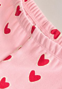 Ljusrosa tygshorts med röda hjärtmönster och vit vågig kant; elastisk midja och mjuk textur.