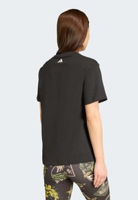 Juoda marškinėliai su apvalia iškirpte, trumpomis rankovėmis ir subtiliu baltu logotipo detalėmis ant nugaros. Pagaminti iš medvilnės, laisvas siluetas.