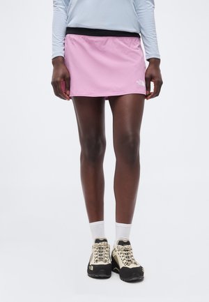 Osoba nosi svetlofialovú športovú sukňu, biele členkové ponožky, béžovo-čierne turistické topánky a svetlomodré tričko s dlhým rukávom.