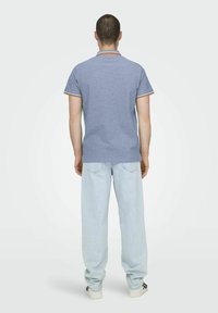 Camisa polo azul claro con cuello a rayas en naranja y blanco, combinada con jeans azul claro de corte suelto y zapatillas blancas.