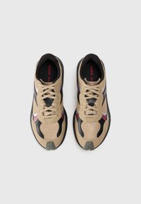 Beige och svarta sneakers med mesh- och lädermaterial; har snörning, strukturerad yta, röda accenter och förstärkt tåhätta.