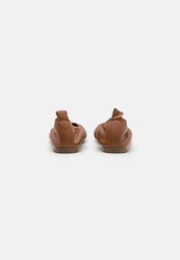 Braune Leder-Balletschuhe mit gerafftem Design, runder Zehenpartie und kleinem Schlaufen-Detail an der Rückseite. Flache Sohle mit minimaler Absatzhöhe.