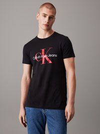Black short-sleeve T-shirt made of cotton, featuring a red "CK" logo and "Calvin Klein Jeans" text in white. Casual fit with rounded neckline.