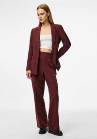 Woman wearing a maroon pinstripe suit with a blazer and matching trousers, paired with a white cropped top and black platform shoes.
