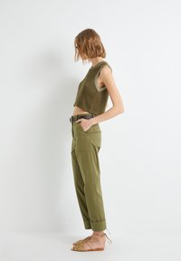 Top en tricot vert olive court sans manches, associé à un pantalon vert olive taille haute et des sandales à lanières tan.