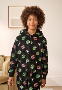 Black hooded onesie made from soft fabric, featuring colorful cartoon patterns of TNT crates and bees. Includes zip closure and cuffs.