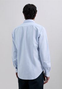 Cămașă albastru deschis cu nasturi, cu dungi verticale fine, mâneci lungi și tiv curbat, realizată dintr-un material neted. Nasturi galbeni vizibili.