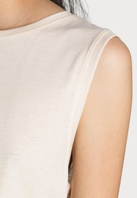 Débardeur beige clair avec une texture douce, encolure ronde et coutures visibles le long des épaules et des emmanchures.