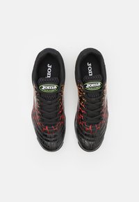 Zapatillas deportivas negras con patrones geométricos en rojo y naranja, superficie texturizada y cordones negros. Logo de la marca visible en la lengüeta y en el lateral.