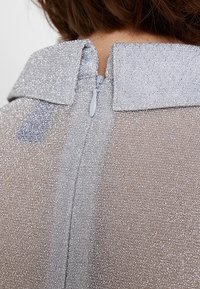 Tissu à texture argentée avec une finition scintillante, présentant un col et une fermeture éclair dissimulée à l'arrière.