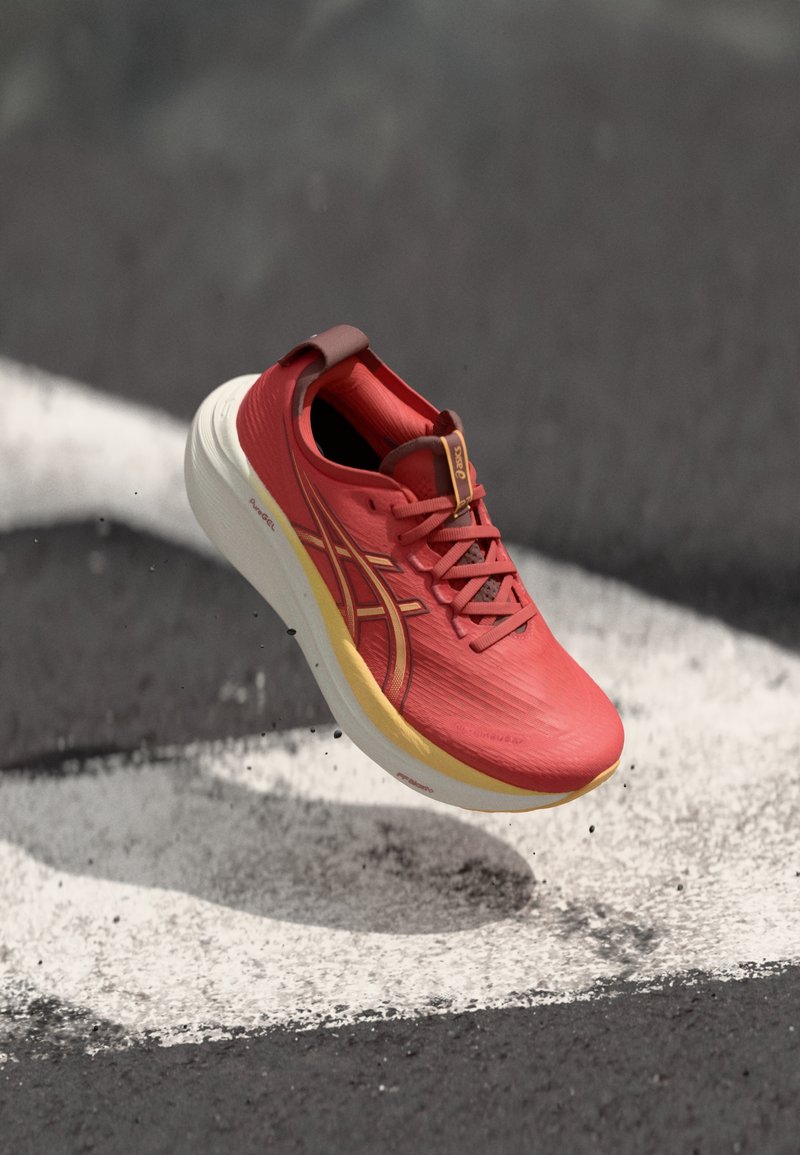 Chaussure de sport rouge avec une tige texturée, design léger, accents jaunes et lacets noirs. La semelle est blanche avec une légère courbure pour le soutien.