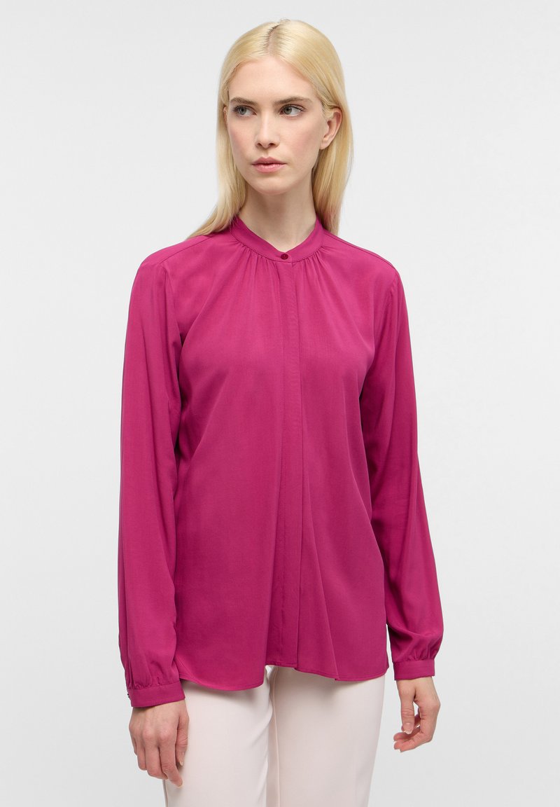 Blusa fucsia a maniche lunghe con colletto rotondo, chiusura con bottoni frontale e dettagli arricciati sulle spalle, realizzata in un tessuto liscio e leggero.