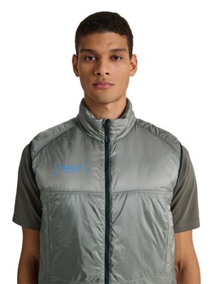 Jonge man draagt een grijs mouwloos doorgestikt vest over een donkergrijs kortemouwen mesh shirt, kijkt recht vooruit met een neutrale uitdrukking.