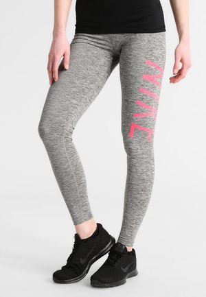 Leggings de sport gris avec une texture chinée, arborant un logo Nike rose sur le côté. Portés avec des chaussures de sport noires.