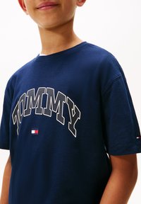Tricou din bumbac de culoare bleumarin, cu un grafic mare în alb ce conține textul "TOMMY". Logo mic brodat pe mâneca stângă. Mâneci scurte și guler rotund.