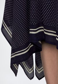 Jupe bleu marine avec des pois blancs et des doubles rayures blanches près de l'ourlet asymétrique, montrant une partie d'une jambe nue.