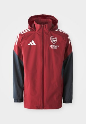 Rød og marineblå treningsjakke med hette, med Arsenal-logo og teksten "Emirates Fly Better", laget av glatt, lett materiale.