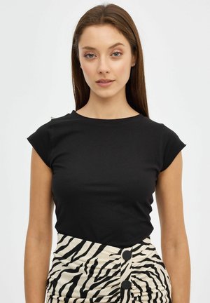 Mujer joven con cabello largo y castaño, vistiendo una blusa negra ajustada sin mangas con cuello redondo y una falda de talle alto con estampado de cebra y dos botones negros.