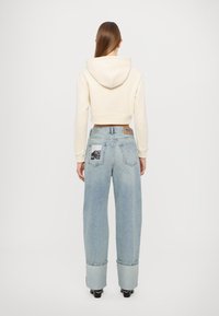 Strihaná béžová mikina v kombinácii s svetloblúzkymi nohavicami s širokými nohavicami, ktoré majú potlačenú nášivku na zadnej vrecku a zatočené manžety.