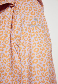 Ūdensizturīga jaka purpursarkanā krāsā ar oranžu leopardu rakstu, ar gludu tekstūru un sudraba krāsu logotipu priekšpusē.