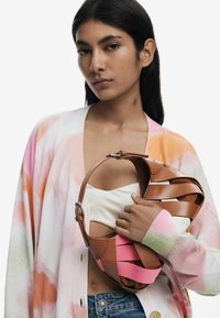 Brown and pink handbag with woven design, smooth leather, featuring a structured handle and accents against a soft, floral-patterned cardigan.