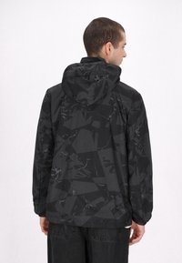 Svart jacka med ett geometriskt mönster i matt och glansigt material, med huva, elastiska manschetter och en avslappnad passform.