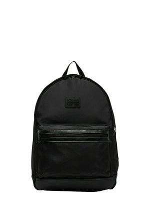 Mochila negra con bolsillo delantero con cremallera, asa superior y una pequeña etiqueta rectangular de marca en el panel frontal superior.