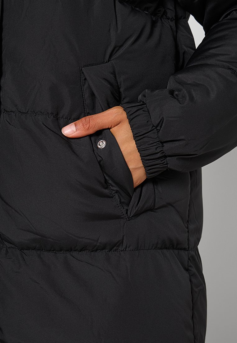 Zwarte pufferjack met een gestructureerde afwerking. Voorzien van een zijzak en elastische manchetten voor een comfortabele pasvorm. De stof lijkt glad en lichtgewicht.