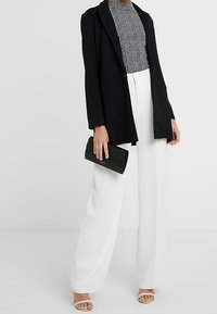 Černý blazer přes texturovaný monochromatický top, zkombinovaný s bílými širokými kalhotami s vysokým pasem a černou kabelkou. Světle zbarvené sandály na pásky.