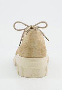 Baskets en suède beige vues de l'arrière, avec une semelle blanche épaisse portant l'inscription "pg" en relief et des lacets beiges noués en un nœud.