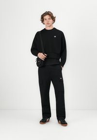 Black sweatshirt with a crew neckline and a logo detail. Paired with black cargo pants featuring multiple pockets. Black sneakers complete the look.