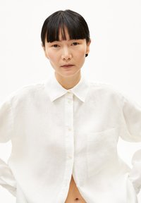 Witte linnen overhemd met puntkraag, enkele borstzak en een comfortabele pasvorm, met een licht gekreukte textuur.