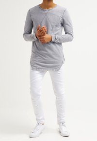 Maglietta grigia a maniche lunghe con collo rotondo e spacchi laterali, abbinata a jeans skinny bianchi strappati con dettagli a coste e strappi.
