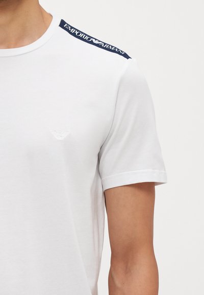 T-shirt in cotone bianco con maniche corte, scollatura a girocollo e un logo navy accento sulla spalla. Sottile emblema del marchio sul petto.