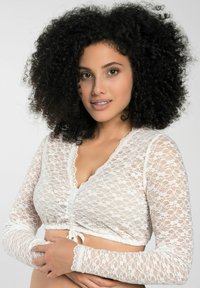 Weißes Spitzen-Crop-Top mit langen Ärmeln, das über einen V-Ausschnitt, einen gerafften Frontbereich und eine dekorative Bindung verfügt. Weiches, strukturiertes Spitzenmuster im ganzen Kleidungsstück.