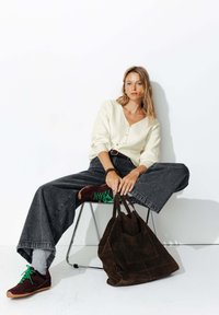 Cardigan en tricot crème clair, jean taille haute gris foncé, baskets bordeaux avec lacets verts, et sac tote en suède marron.