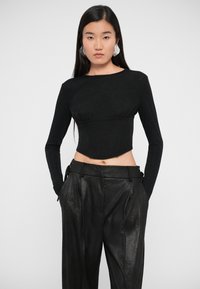Black long-sleeve top in a fitted design with a textured finish, paired with loose black pants featuring side pockets and belt loops.