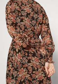 Pitkähihaista, mustaa kukkakuosiset mekkoa, jossa on vaaleanpunaisia ja beigejä kukkia, kerätyt hihansuut ja rento istuvuus.