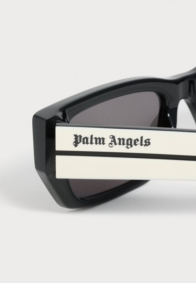 Lunettes de soleil rectangulaires noires avec de grosses branches blanches portant l'inscription "Palm Angels" en caractères noirs Old English.