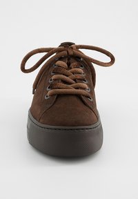 Baskets en daim marron avec semelle épaisse et foncée, bout arrondi et larges lacets noués, vues de face sur un fond uni.