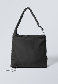 Black fabric tote bag with a textured finish, featuring a wide strap and side lace detailing. Large main compartment with top zipper closure.